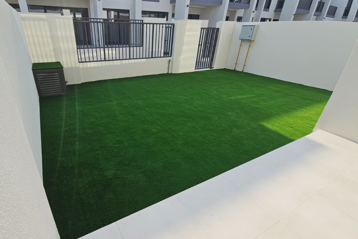 Modern courtyard with artificial grass enclosed by white walls and black metal fencing, surrounded by buildings.