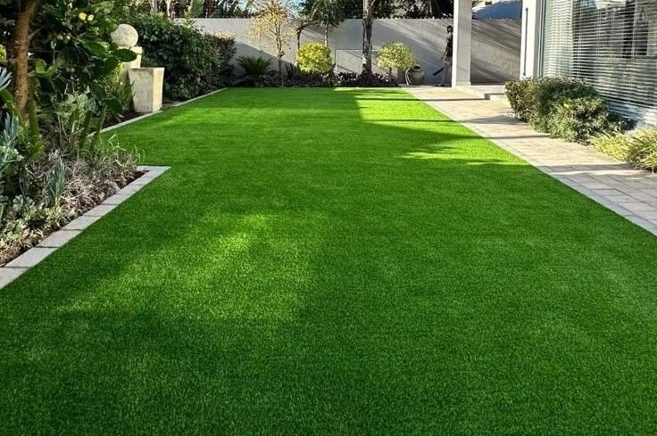 Well-manicured green lawn in a modern garden with paved walkway and surrounding plants.