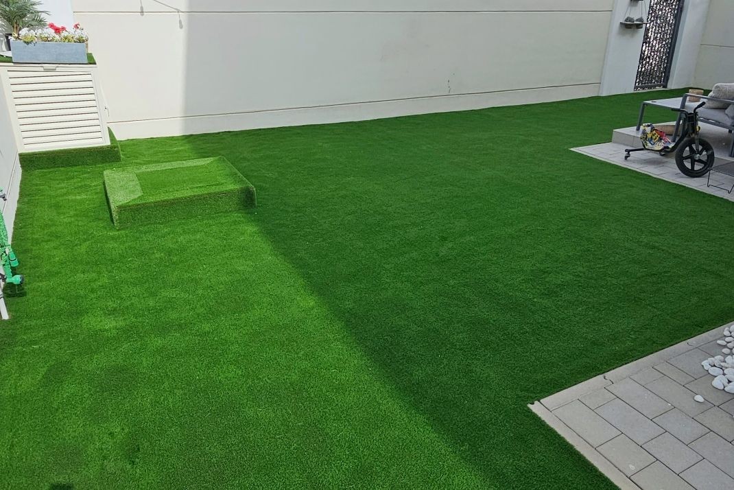 Outdoor space with green artificial grass, patio furniture, and modern white buildings in the background.